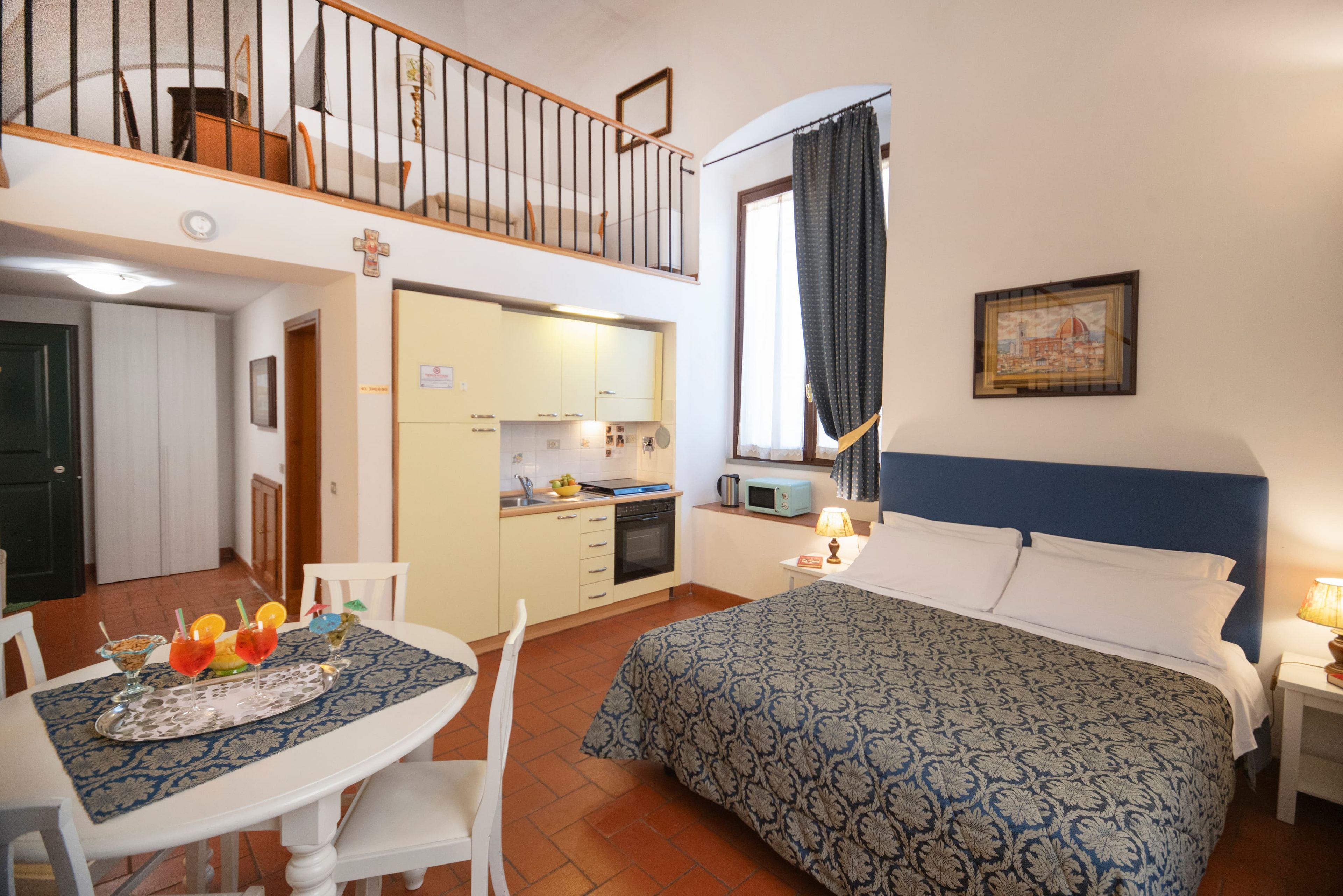 A bedroom with a bed, a dining table with chairs, a kitchen area, and a balcony.