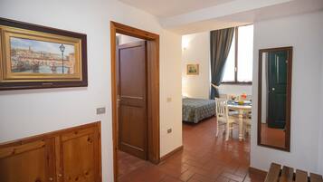 Un pasillo con puerta de madera, un cuadro enmarco, una cama con colcha estampada y una mesa de comedor con sillas.