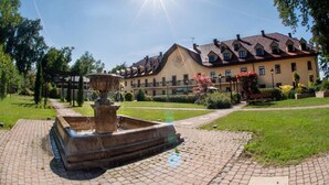 A courtyard with a fountain, a large building with a clock, and a clear sky. - Turowka Hotel & Spa (Wieliczka)