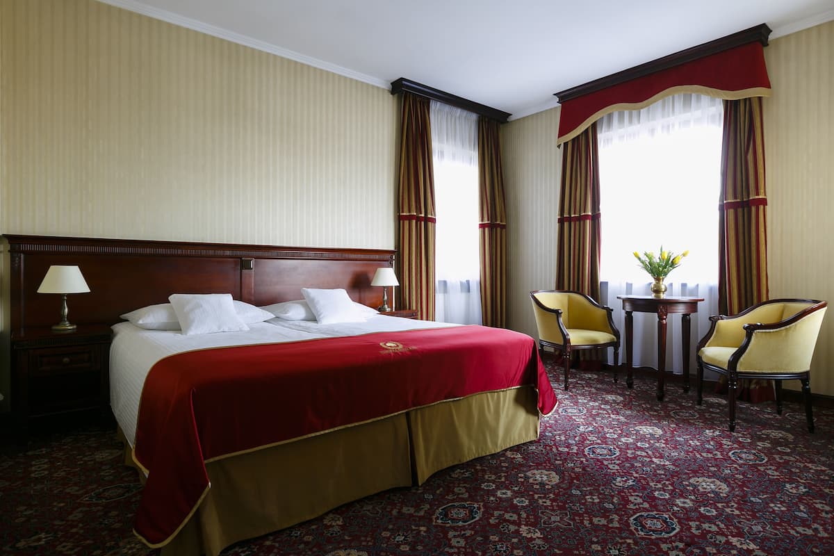 Ein Hotelzimmer mit einem großen Bett, zwei Sesseln, einem kleinen Tisch und einem Fenster mit Vorhängen.