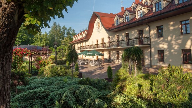 A traditional building with a balcony, surrounded by lush greenery and a well-maintained garden. - Turowka Hotel & Spa (Wieliczka)