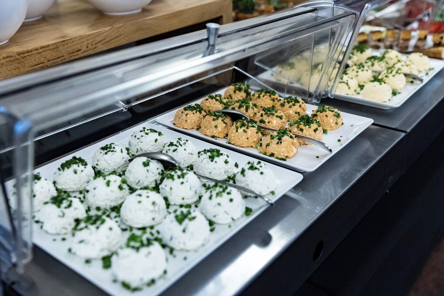 Un bufé con diversos alimentos, incluyendo fuentes blancas y marrones decoradas con hierbas verdes.