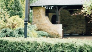 A gazebo with a stone exterior and a tiled roof, surrounded by lush greenery and a tall, ornate street lamp. - Turowka Hotel & Spa (Wieliczka)