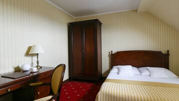 Hotellihuone, jossa on sänky, kirjoituspöytä lampun kanssa, tuoli ja vaatekaappi.