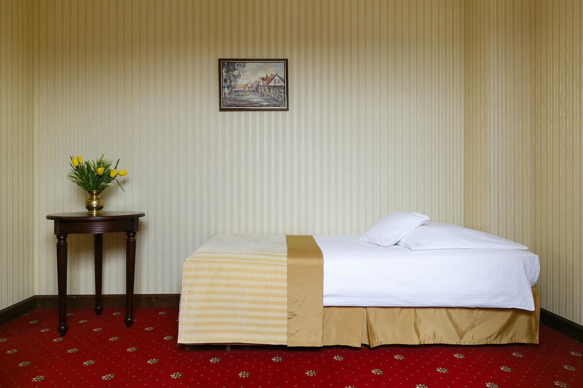 Ein Hotelzimmer mit einem Bett, einem kleinen Tisch mit Blumenvase und einem gerahmten Bild an der Wand.