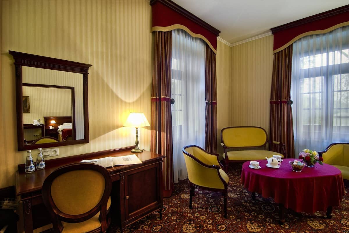 Ein Hotelzimmer mit einem großen Spiegel, zwei Stühlen, einem kleinen Tisch mit roter Tischdecke und einem gemusterten Teppich.