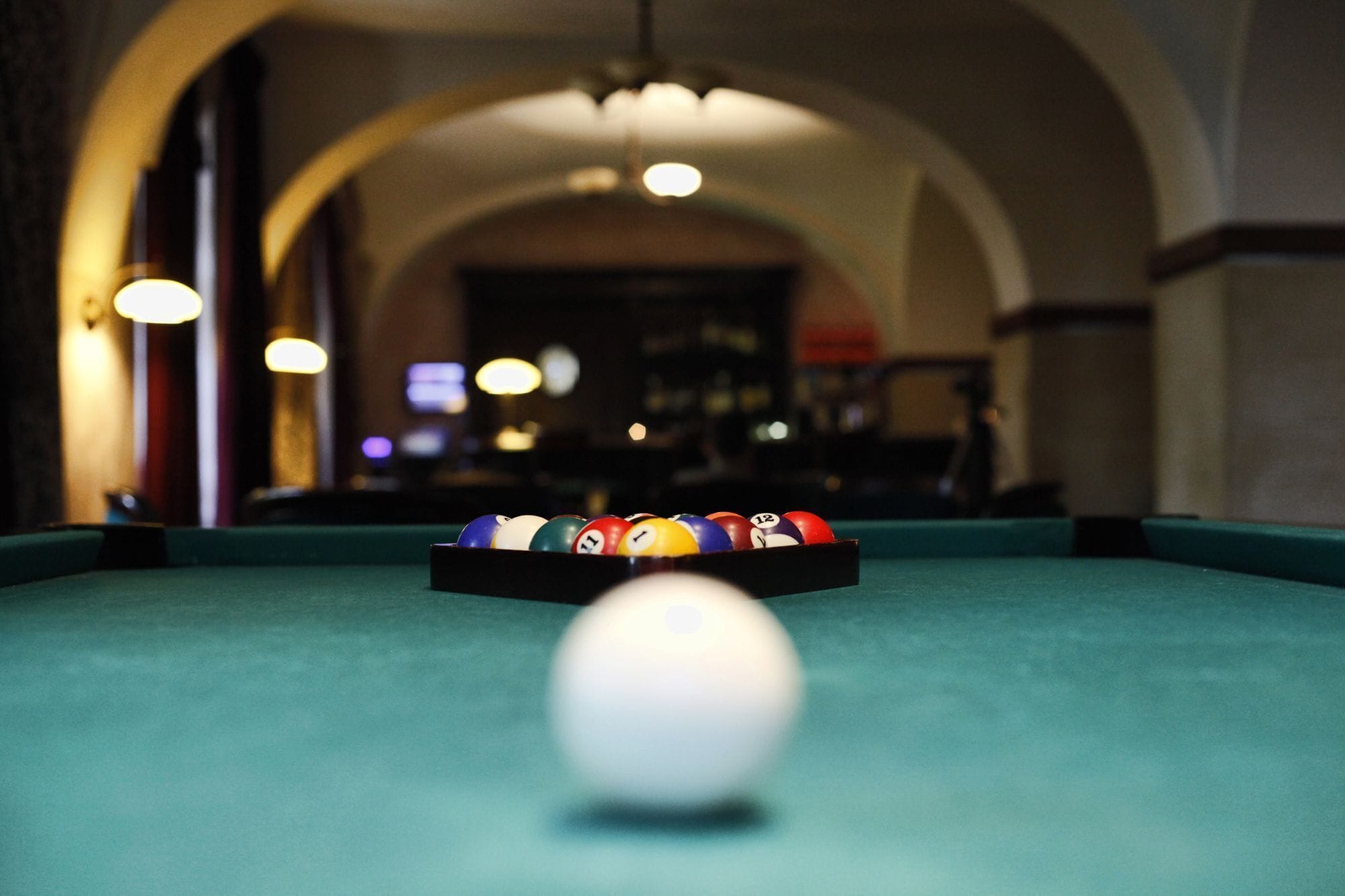 Una mesa de billar con bolas en primer plano y una zona de bar al fondo.