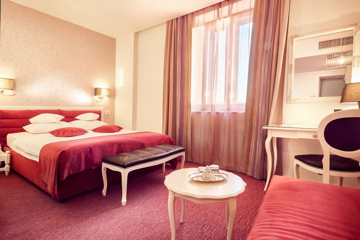 A hotel room with a large bed, a desk, a chair, and a small table.