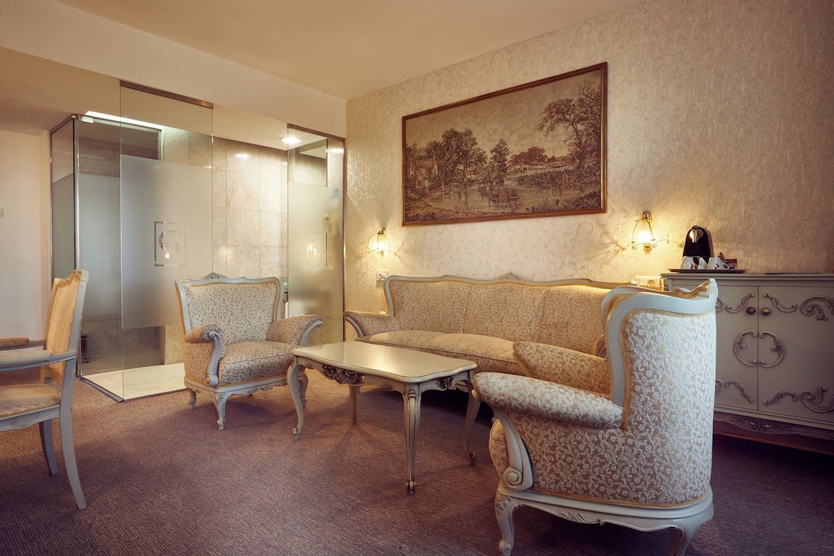 A room with a sofa, two armchairs, a small table, a cabinet, and a painting on the wall.