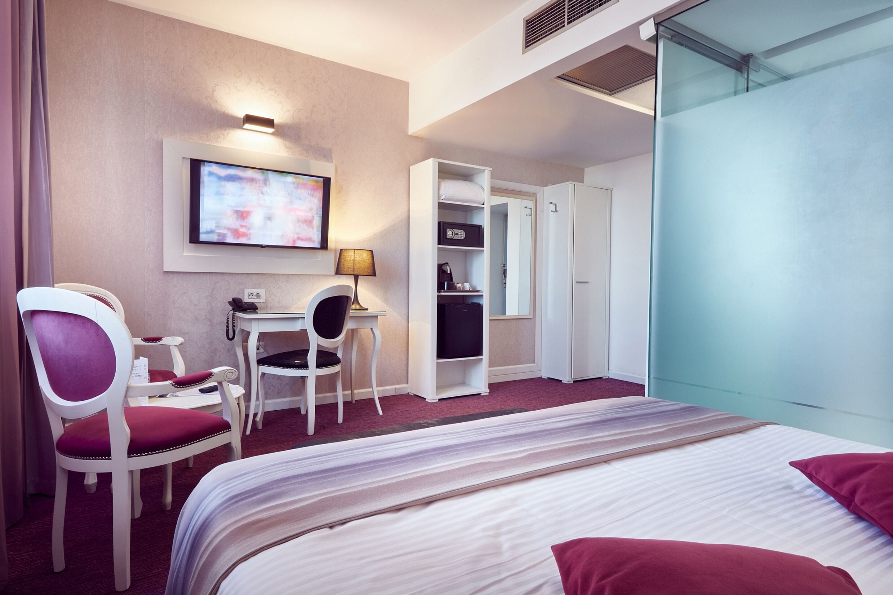 A hotel room with a bed, a desk, a chair, a television, and a wardrobe.