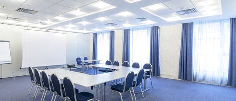 Un salón de conferencias con una larga mesa, sillas, una pizarra y ventanas amplias con cortinas.