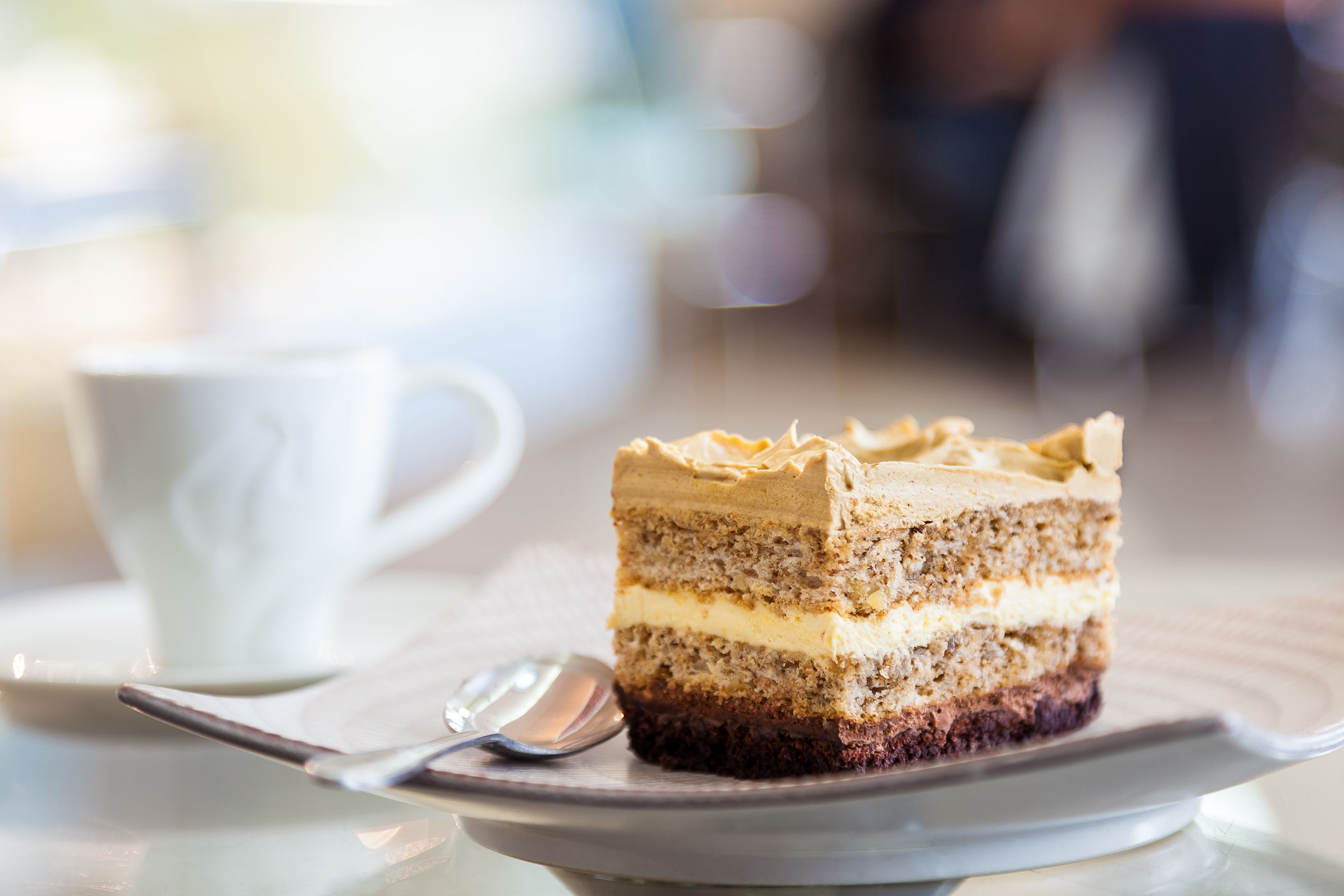 A slice of layered cake on a white plate with a spoon beside it, placed on a table.