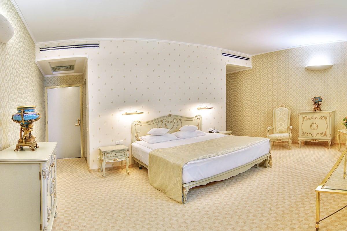 A classic bedroom with a large bed, bedside tables, a wardrobe, and a mirror.