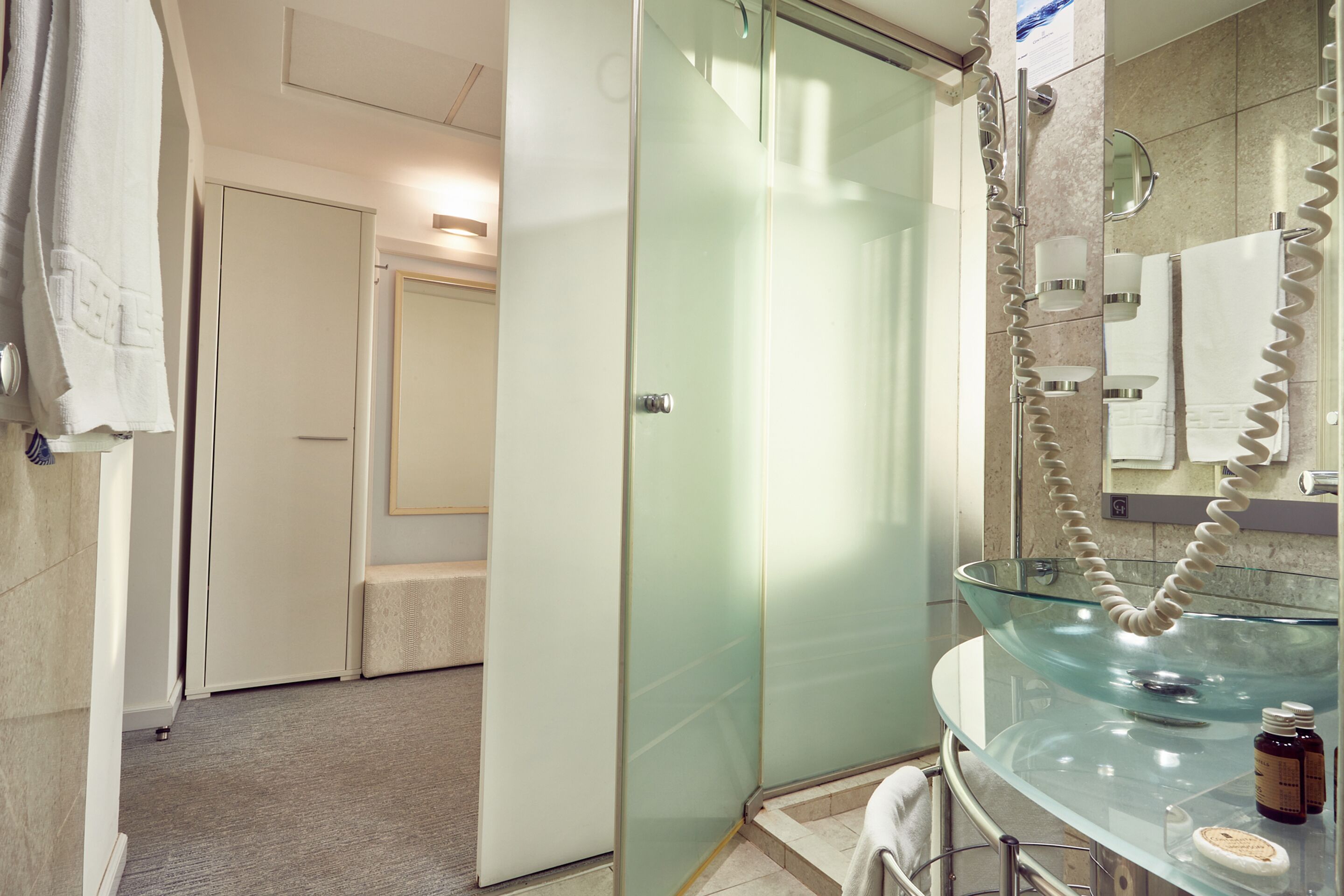 Une salle de bain moderne avec un lavabo en verre, une cabine de douche en verre et un miroir doté d’un porte-serviettes.