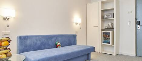 A room with a blue sofa, a glass table with fruit, a microwave, and a mini fridge.