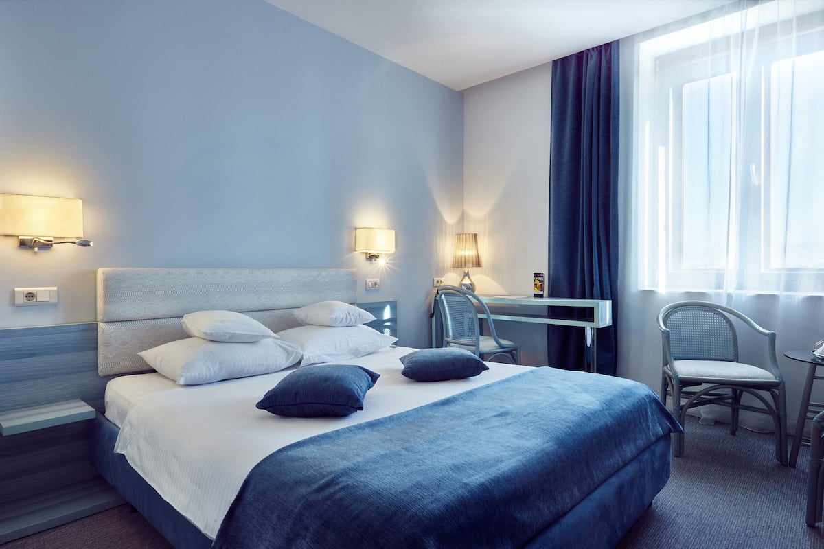 A modern hotel room with a large bed, two bedside tables, a desk, and a chair.