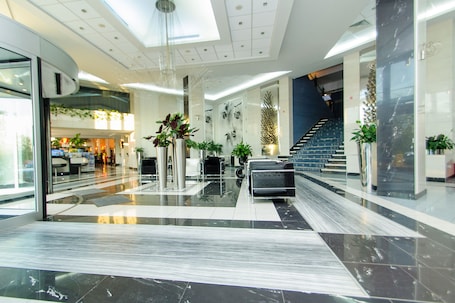 A modern lobby with a marble floor, a staircase, and several potted plants.