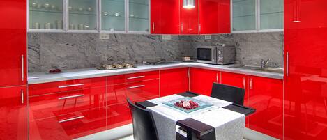 A modern kitchen with red cabinets, a microwave, and a dining area with a table and chairs.