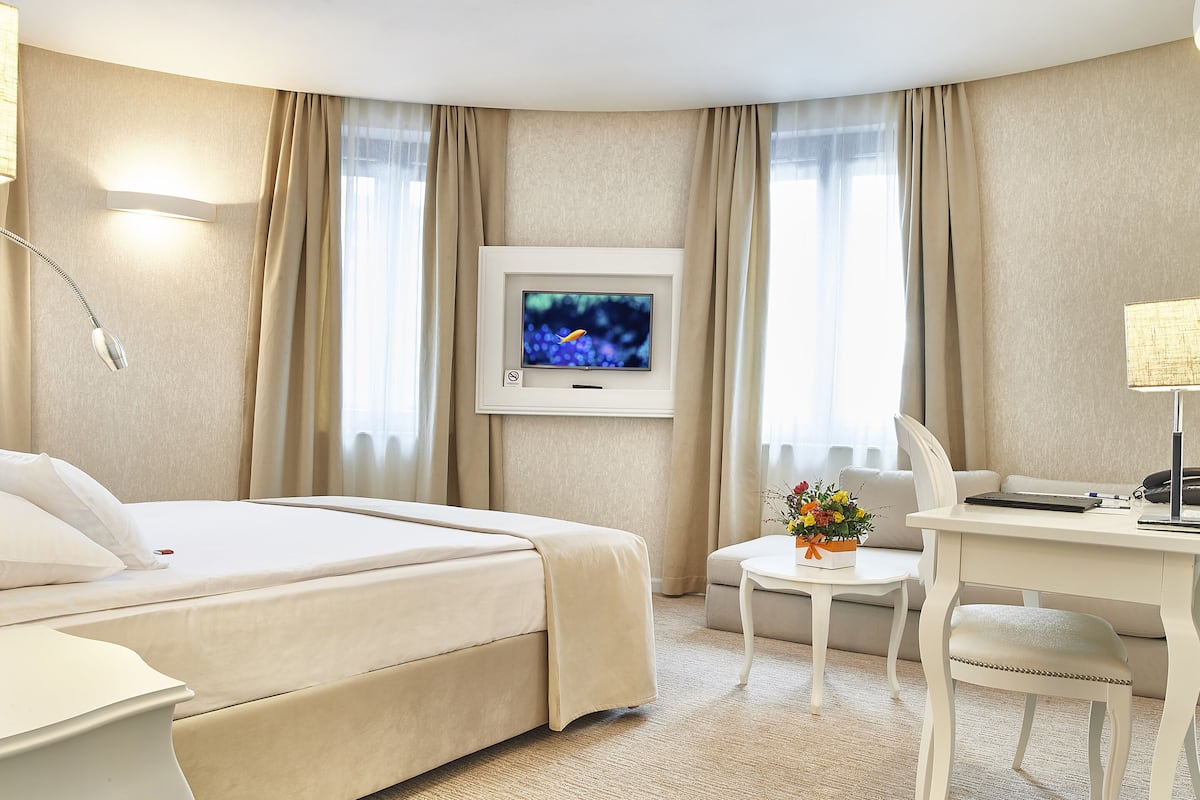 A hotel room with a bed, a desk, a chair, a television, and a small table with a flower arrangement.