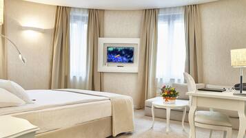 A hotel room with a bed, a desk, a chair, a television, and a small table with a flower arrangement.