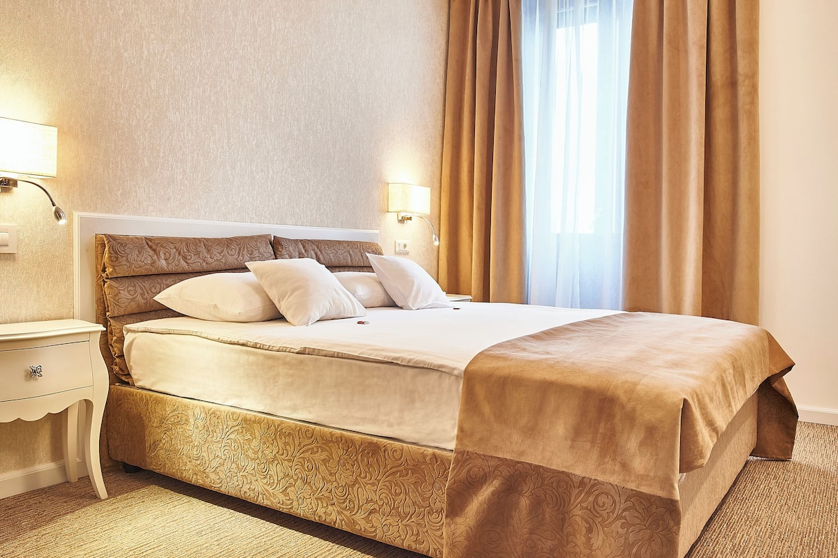 A neatly made bed with a patterned bedspread, a bedside lamp, and a nightstand with a drawer.