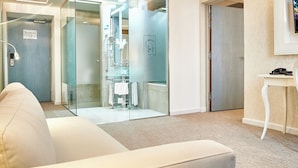 A modern hotel room with a glass partition, a white sofa, a small table with a phone, and a framed picture on the wall. - Continental Forum Sibiu (Sibiu)