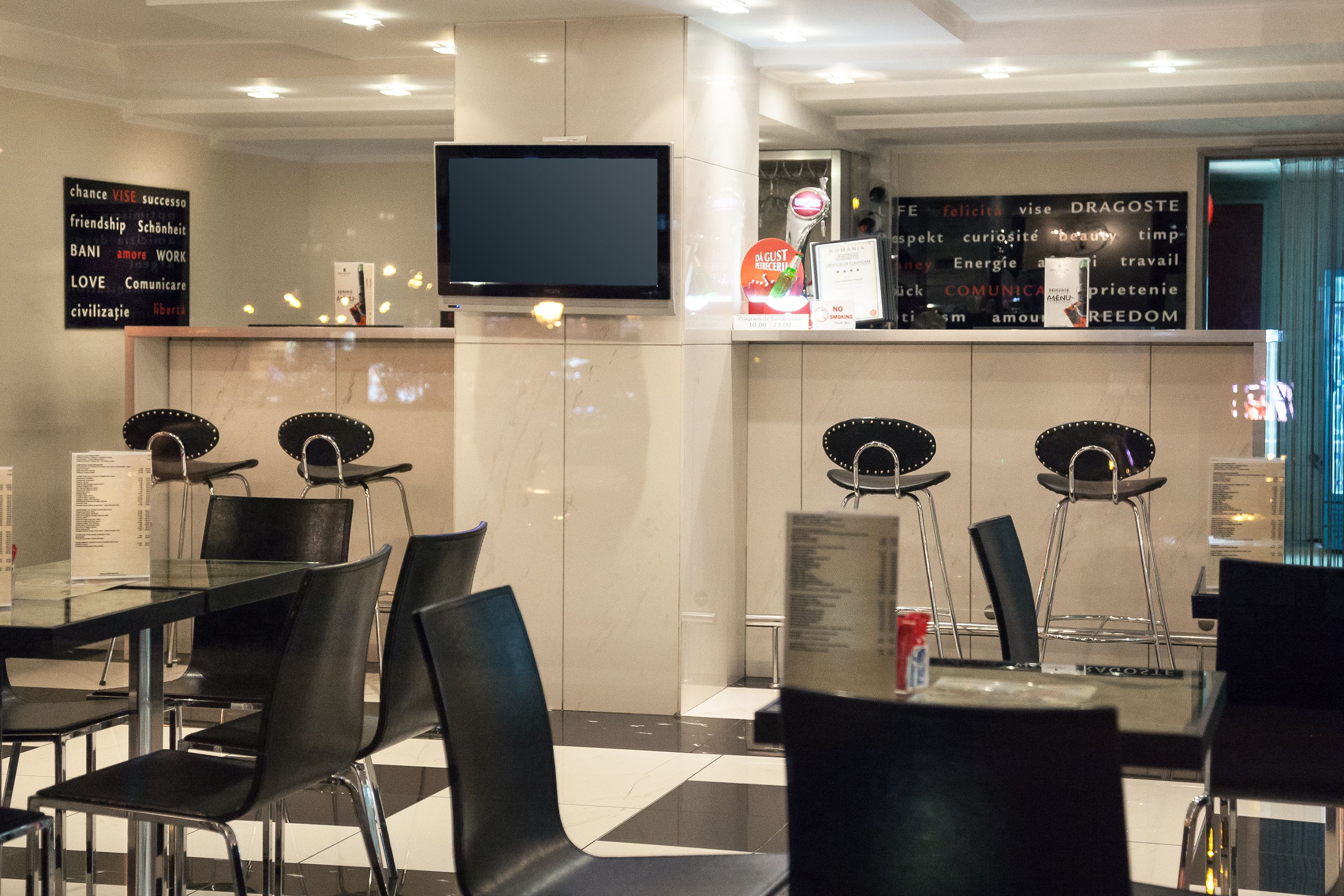 Un restaurante moderno con sillas y mesas negras, un televisor de pantalla plana en la pared y carteles motivacionales.