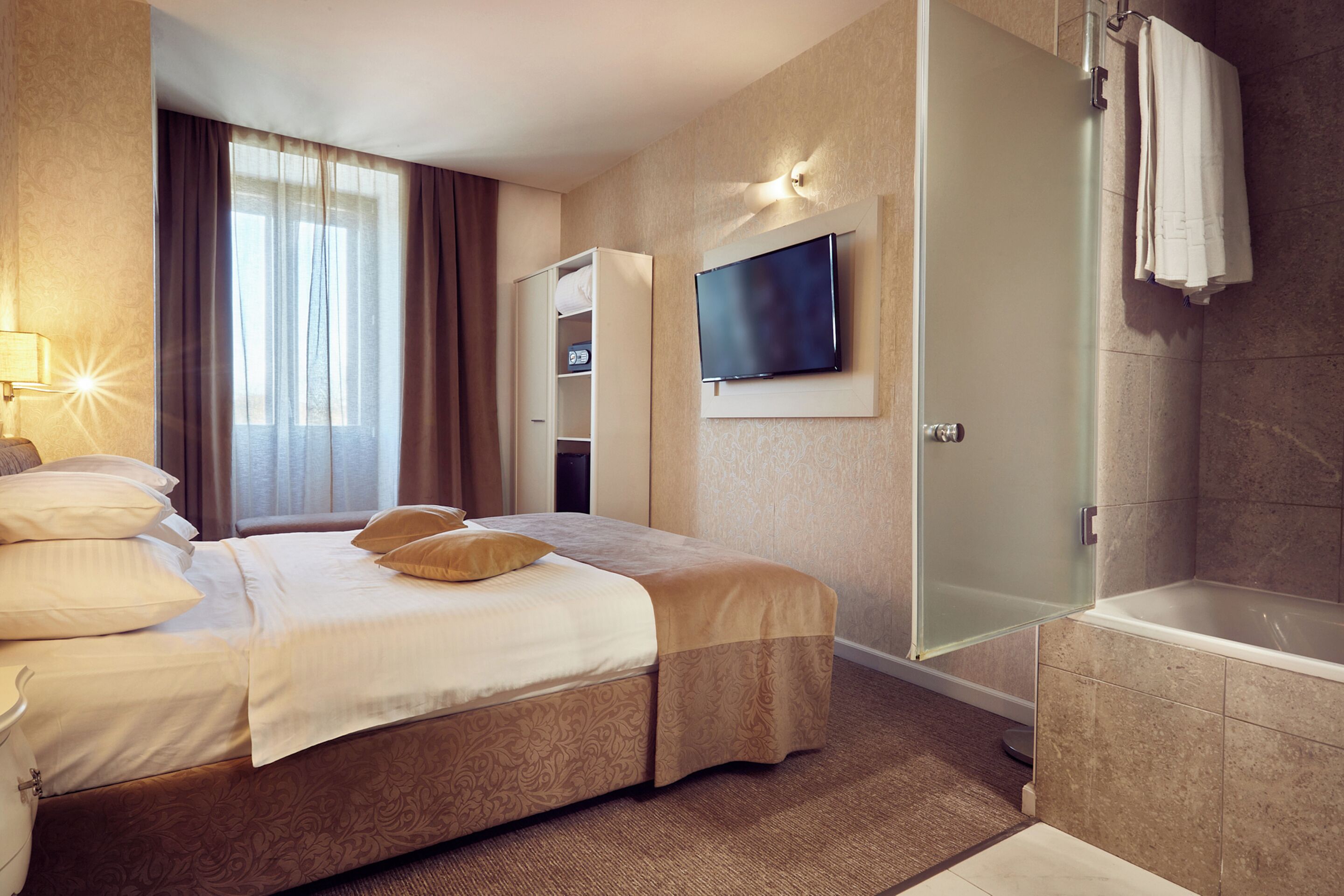 A hotel room with a bed, a TV, a shower, and a wardrobe.