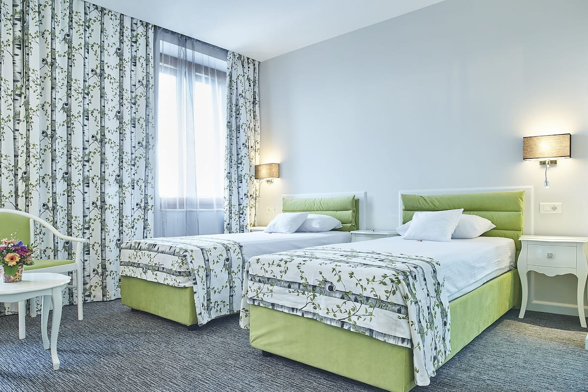 A hotel room with two beds, a desk, a chair, and a window with curtains.