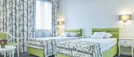 A hotel room with two beds, a desk, a chair, and a window with curtains.