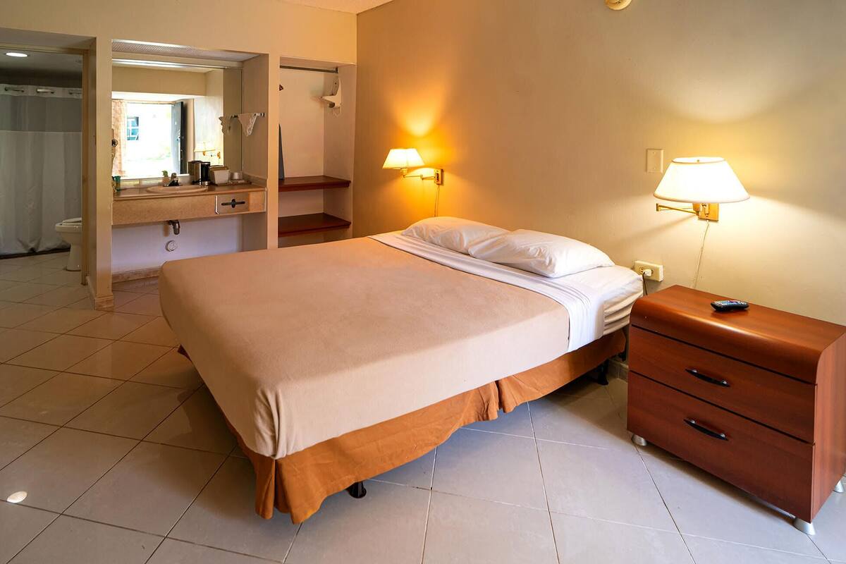 Une chambre d’hôtel comprenant un lit, des tables de chevet, un miroir et une petite table de nuit avec une lampe.