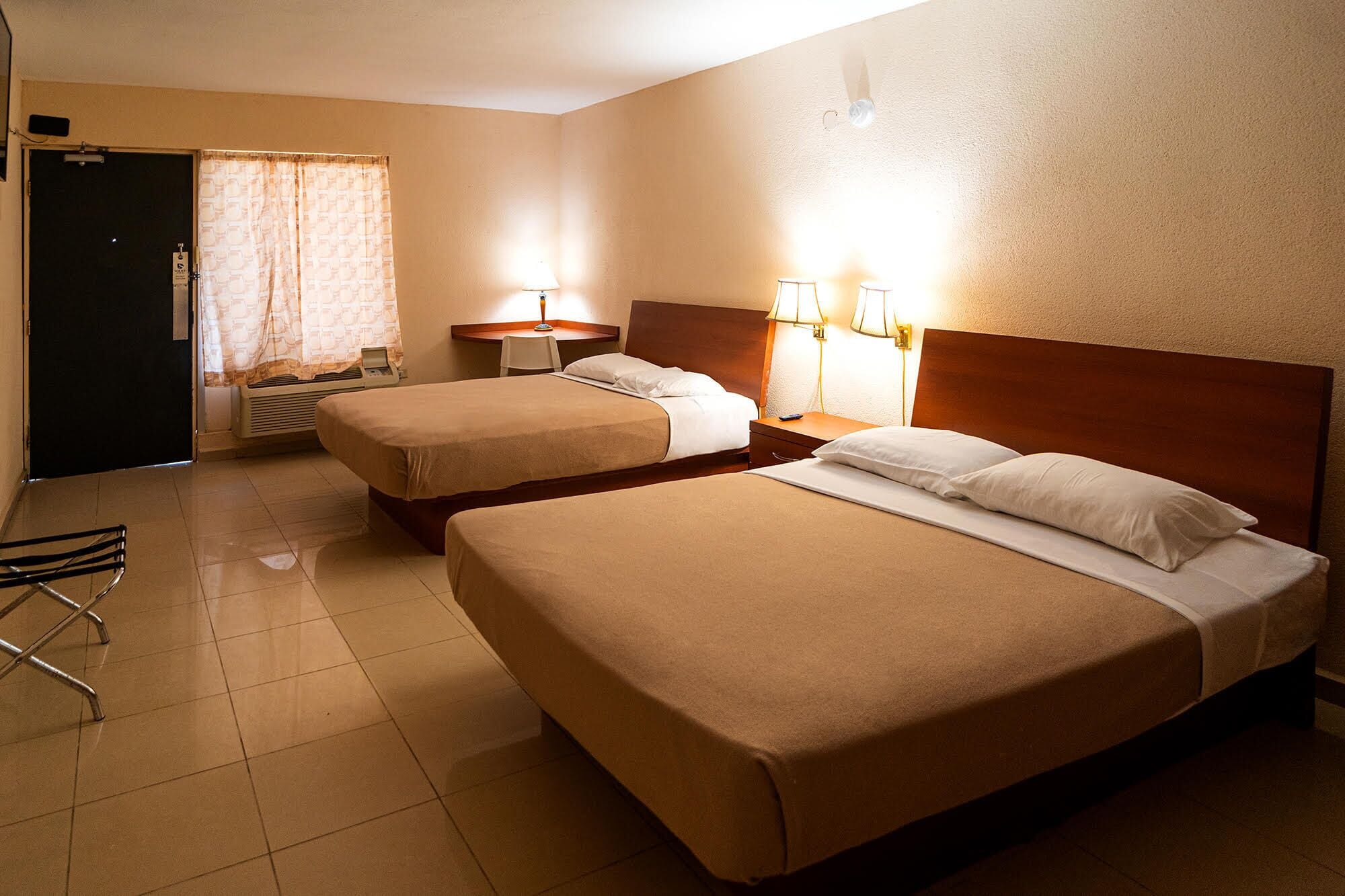 A hotel room with two beds, a desk, a chair, and a window with curtains.