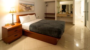 Un dormitorio con cama, mesita de noche, lámpara y un cuadro de una escena de playa.