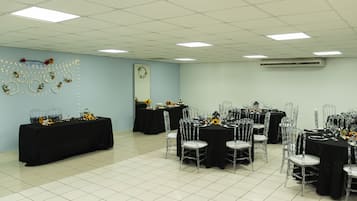 A conference room with multiple tables and chairs, a ceiling with fluorescent lights, and an air conditioning unit on the wall.