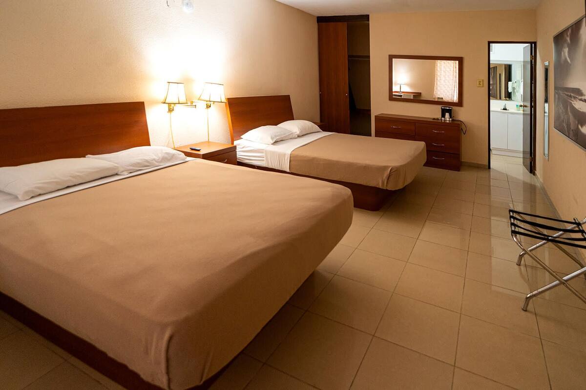Une chambre d’hôtel avec deux lits, une table de chevet avec une lampe, une commode et un miroir.