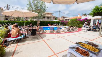 Ein Poolbereich mit Liegestühlen, Sonnenschirmen und einem Buffet mit Speisen.