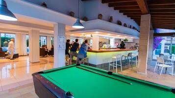 A pool table in a well-lit indoor area with a bar and seating.
