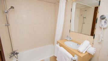 A bathroom with a bathtub, a sink, a mirror, and a hairdryer.