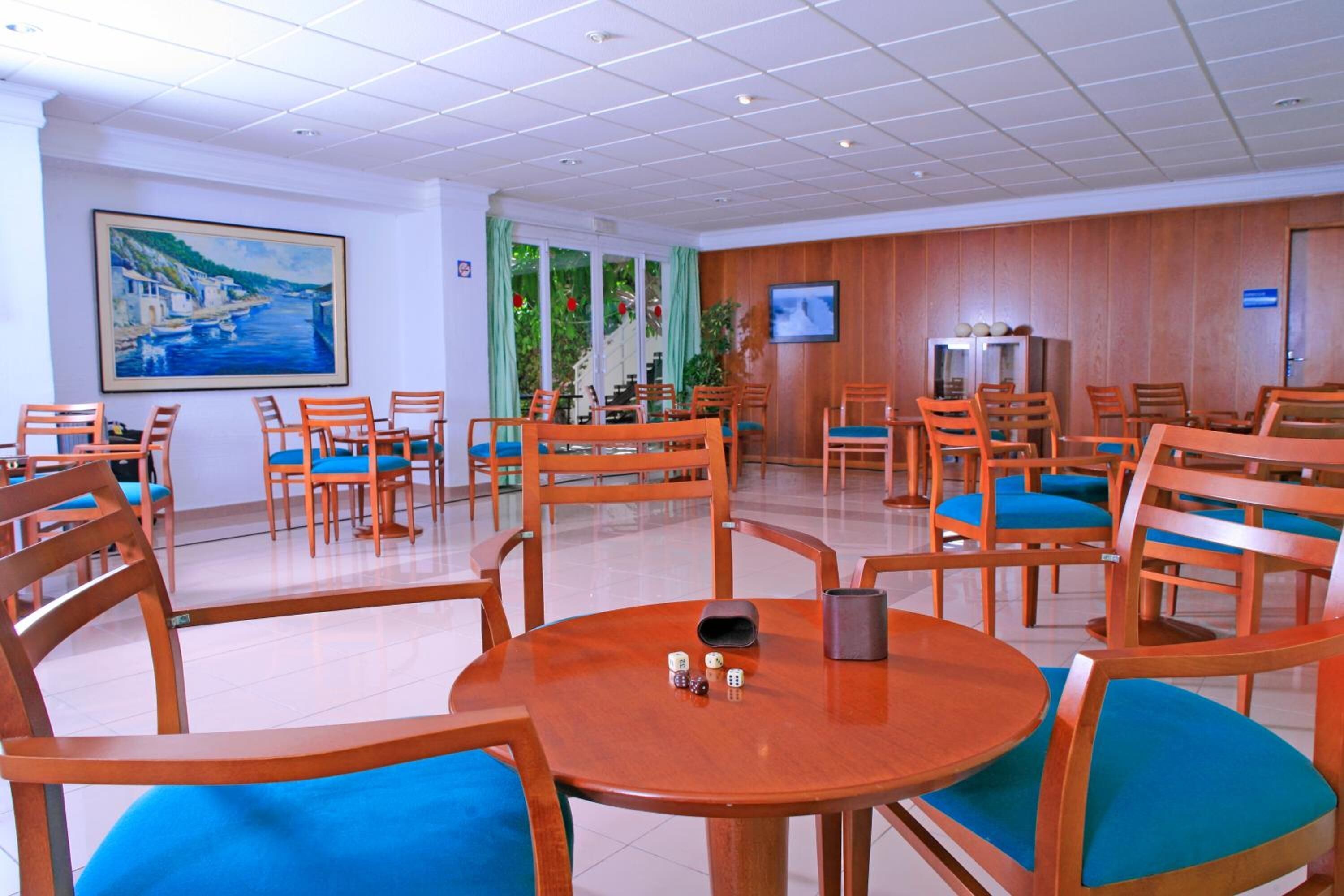 Un hall de hotel con varias mesas y sillas de madera, un cuadro grande en la pared y una pantalla de televisión.