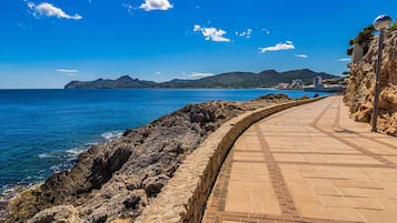 Un paseo marítimo con un muro de piedra a un lado y una vista despejada del mar y montañas distantes.