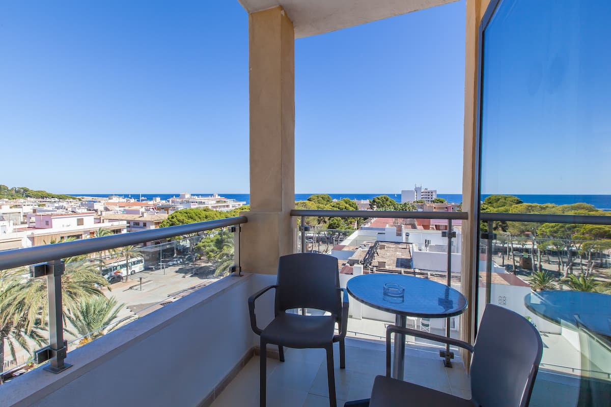A balcony with a table and chairs, offering a view of the city and the sea.