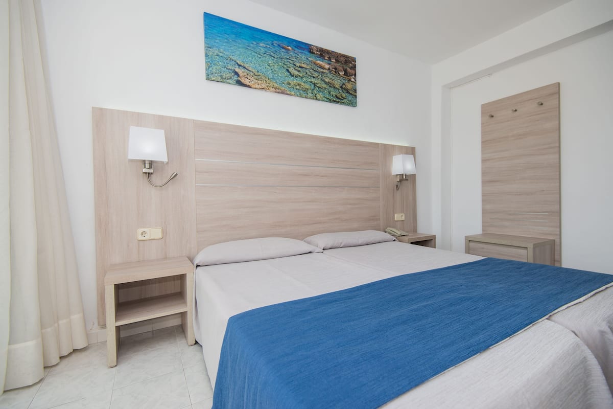 A hotel room with a large bed, two bedside tables, a nightstand, a wall-mounted lamp, and a painting above the bed.