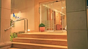 Entrada d'hotel amb un disseny modern, que inclou una escala, una planta en test i una porta de vidre que dona accés a l'interior.