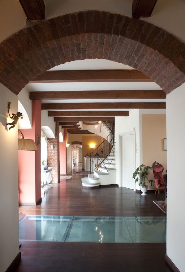 A spacious interior with a glass floor, brick archway, wooden beams, a staircase, and a white door.