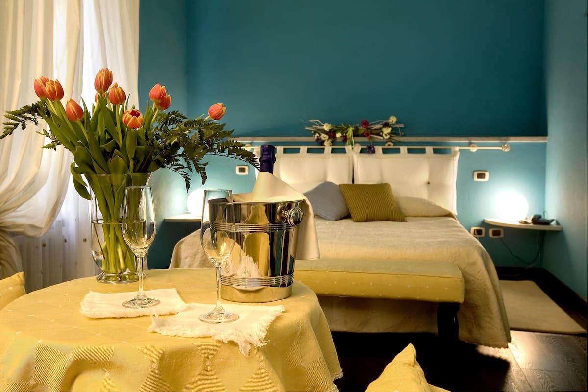 Habitación de hotel con una cama, una mesita de noche con un florero, un cubo y un vaso de agua.