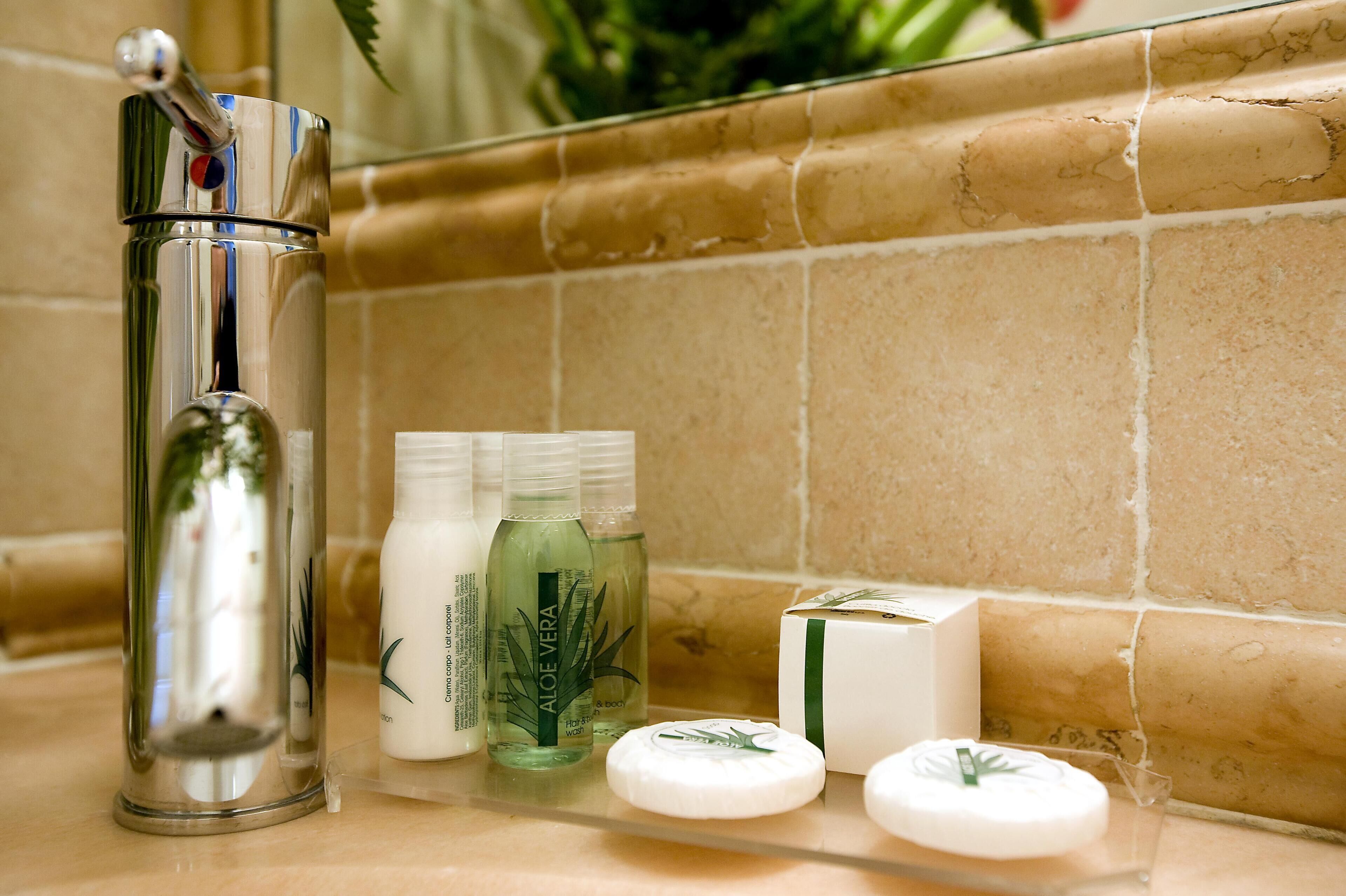 Ein Badezimmer-Waschtisch mit einem chromfarbenen Wasserhahn, Flaschen mit Aloe Vera und einem weißen Seifenstück.
