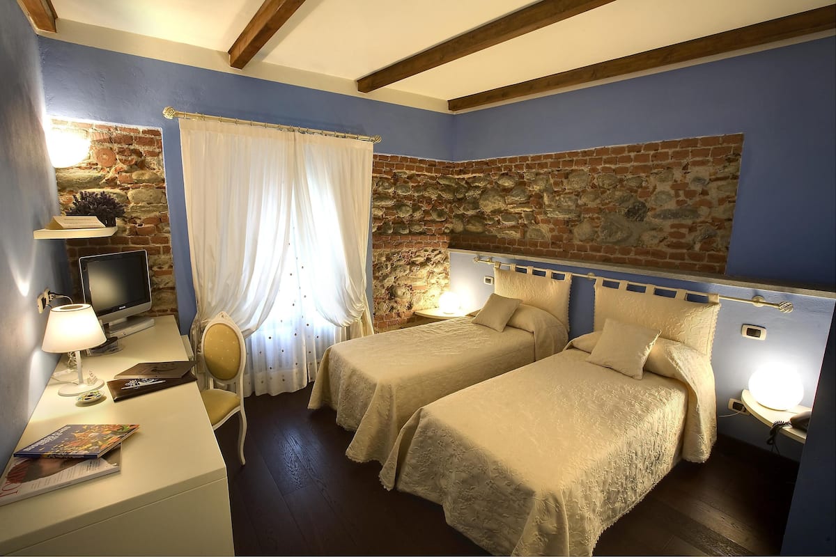 Una habitación con dos camas, un escritorio con computadora, un televisor y una pared de piedra.