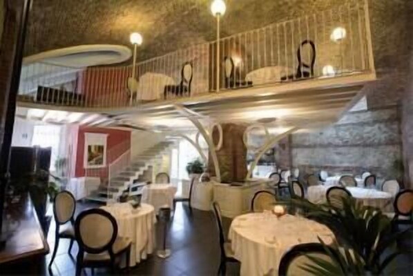 A restaurant with round tables, chairs, and a staircase leading to an upper level.