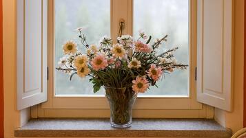 Ein Essbereich mit Tisch und Stühlen, ein Blumenstrauß auf einer Fensterbank und Blick ins Freie.