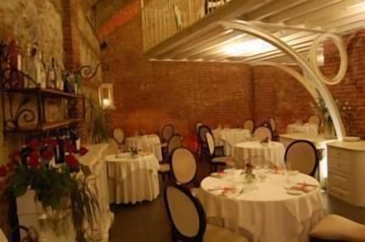 A restaurant with round tables and chairs, white tablecloths, and a brick wall interior.